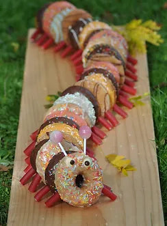 Decorated donuts arranged in the shape of a caterpillar, with lolly detailing for legs,  eyes and feelers